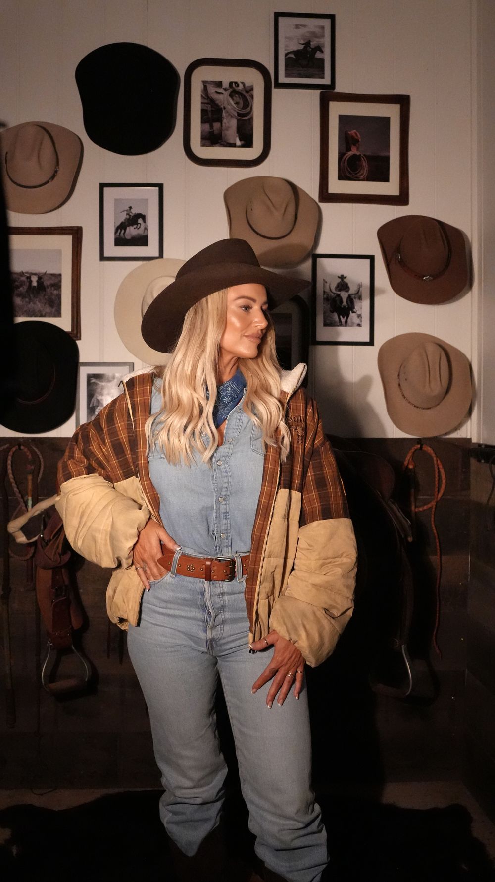 Cowgirl posing in front of a wall of hats